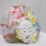 A sculpture of a face attached to a ball of newspaper with a pill in its mouth .